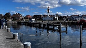 A waterfront pier with a lighthouse, docked boats, and residential buildings in the background. - Cozy semi-detached house with fireplace and terrace close to the Baltic Sea (Hohenkirchen)