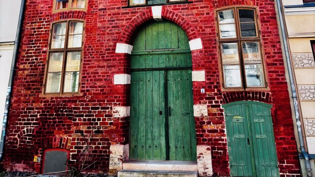 A red brick building with a green door and multiple windows. - Cozy semi-detached house with fireplace and terrace close to the Baltic Sea (Hohenkirchen)