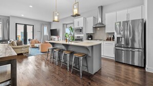 A modern kitchen with a central island, stainless steel appliances, and a bar stool seating area. - Above the Gulch • Rooftop Fire Pit • Skyline Views (Nashville)