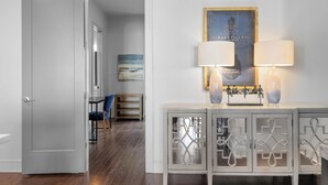 A hallway with a white door, a blue chair, a small table, and a cabinet with decorative glass doors. - Above the Gulch • Rooftop Fire Pit • Skyline Views (Nashville)