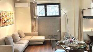 A modern living room with a sofa, a glass dining table set with plates and glasses, a floor lamp, and a window with curtains. - Check in information:You won’t need to meet anyone to access the apartment. Before arrival, you will receive a link to access the Guest Portal, where you can complete the self check-in directly from your phone by entering the ID details of all guests a (Milano)