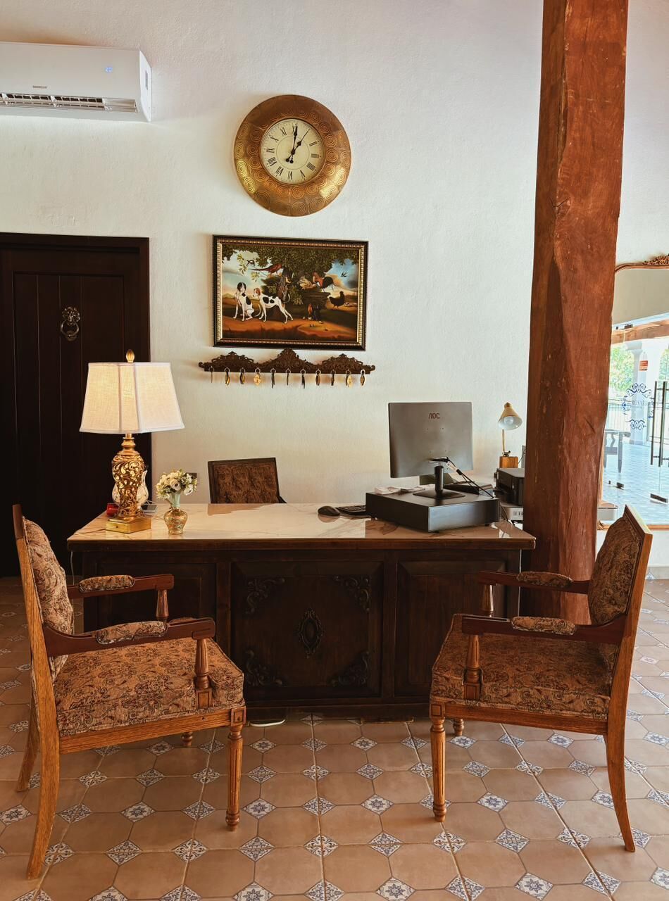 A room with a desk, two chairs, a clock, a framed picture, and a large wooden column.