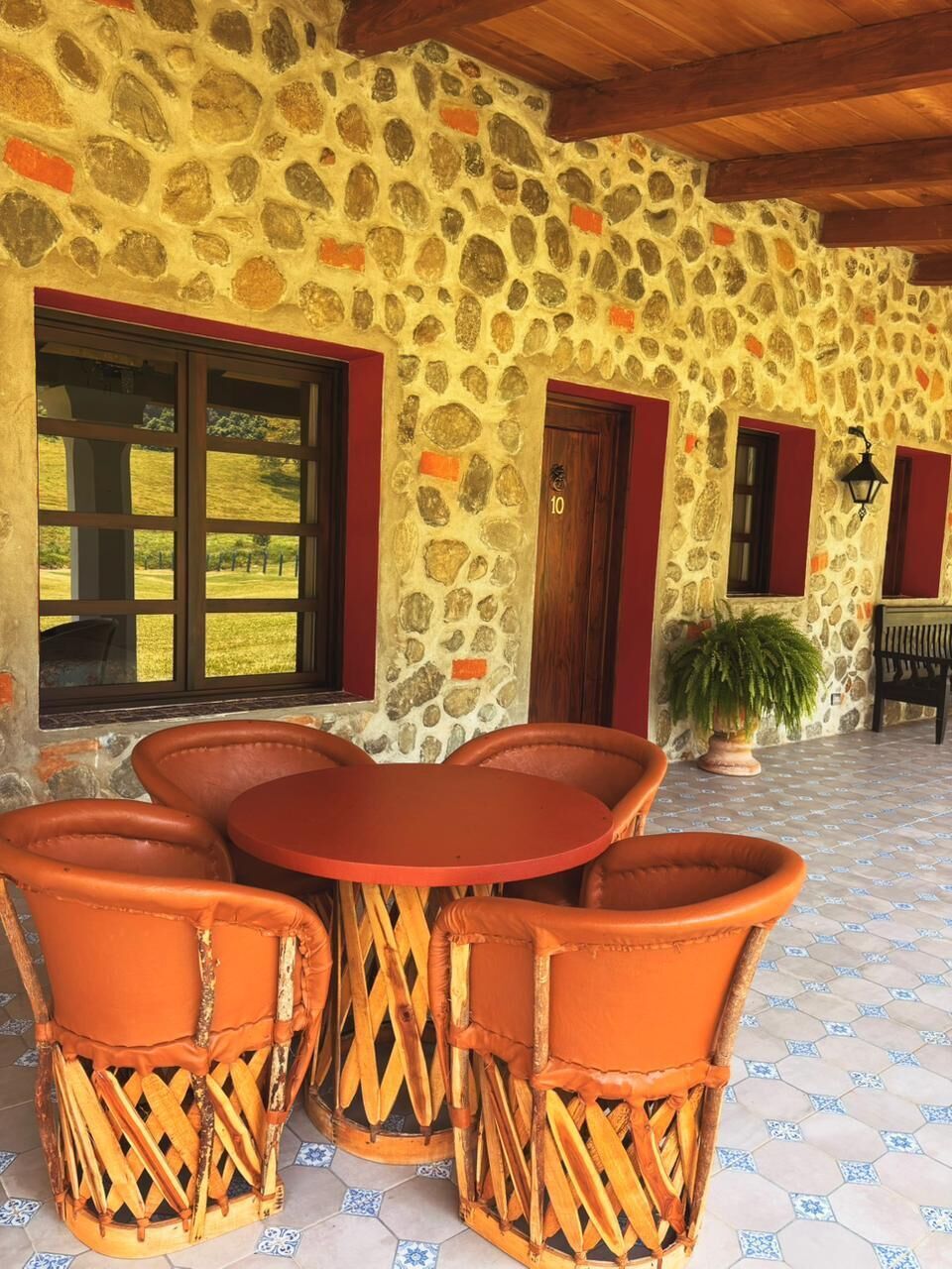 A stone building with a wooden ceiling, a round table with chairs, and a potted plant.