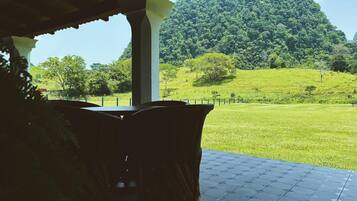 A covered outdoor seating area with a view of a green field and a hill.