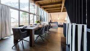 Ein Essbereich mit Holztisch und Stühlen, großen Fenstern und Blick ins Freie.
