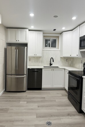 A modern kitchen with white cabinets, stainless steel appliances, and a window above the sink.