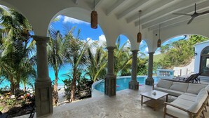 A covered outdoor area with a pool, seating, and palm trees. - White Sand Beachfront - Brand New Peter Bay "Villa La Playa" (St John)