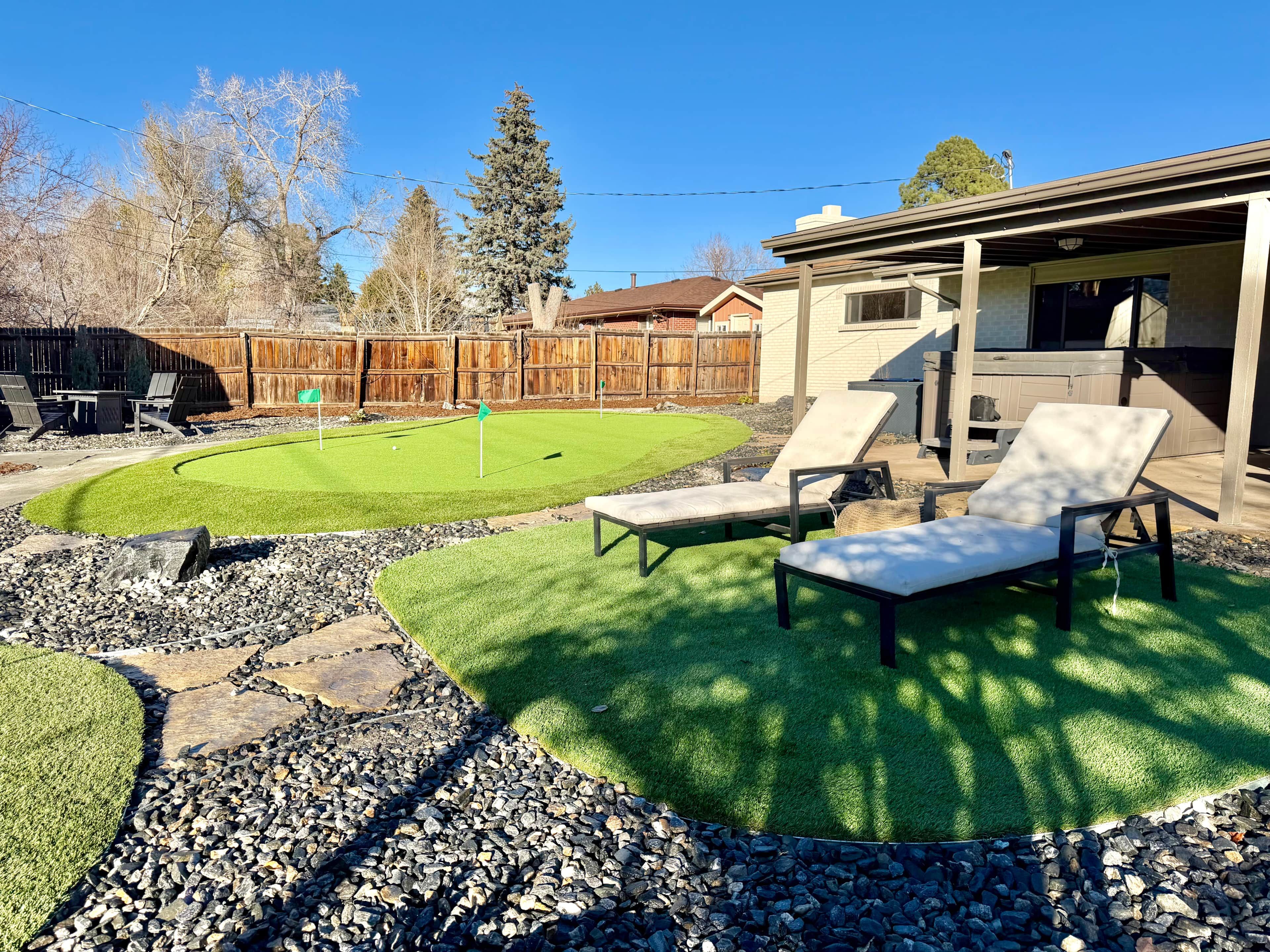 A backyard with a lawn, two lounge chairs, a wooden fence, and a house.