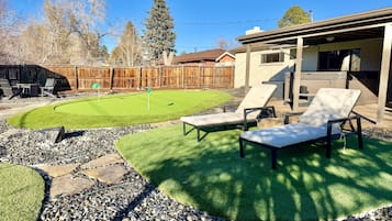 A backyard with a lawn, two lounge chairs, a wooden fence, and a house.