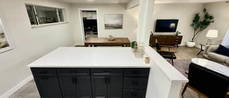 A modern kitchen with a large island, dark cabinetry, and a dining area with a wooden table.