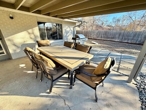 An outdoor patio with a table and chairs, a barbecue grill, and a view of a backyard. - Family Fun Hub • Games, Hot Tub, Putting Greens (Centennial)