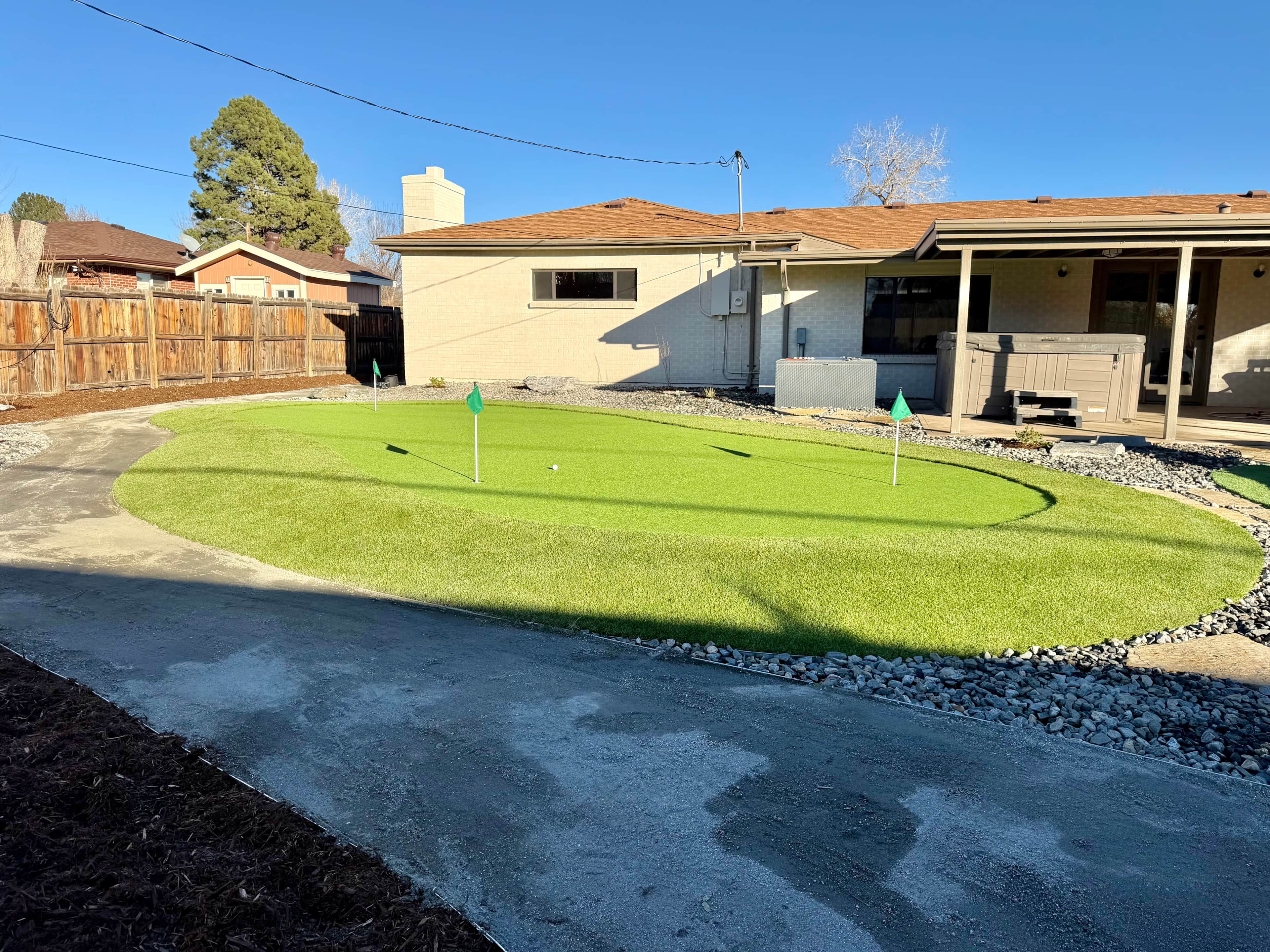 A residential backyard with a lawn, a hot tub, and a wooden fence.