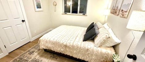 Une chambre à coucher avec un lit, une fenêtre, une lampe fixée au mur et une porte.