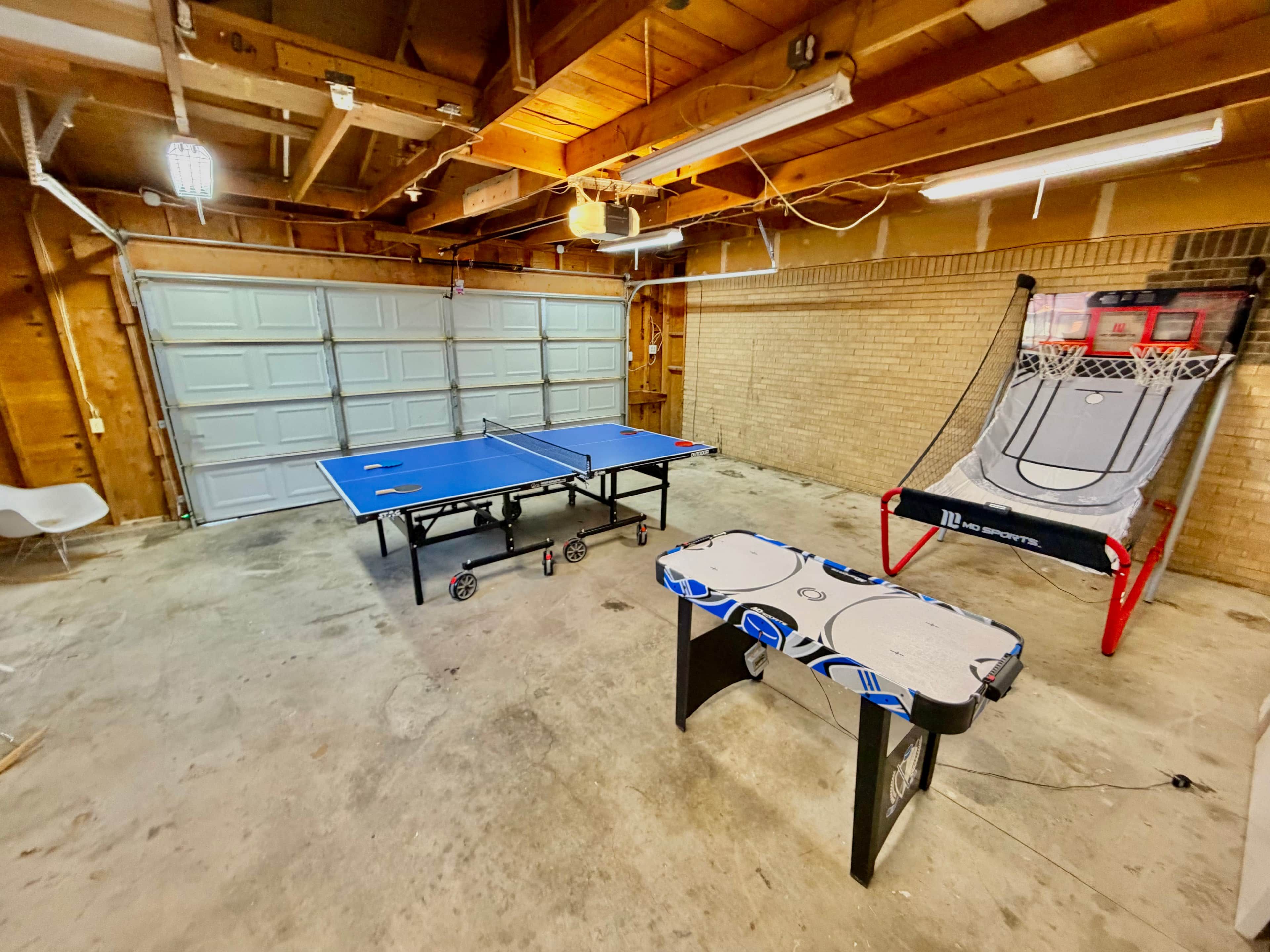 A room with a ping pong table, a basketball hoop, and a table tennis table.