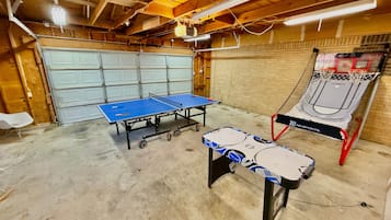 A room with a ping pong table, a basketball hoop, and a table tennis table.