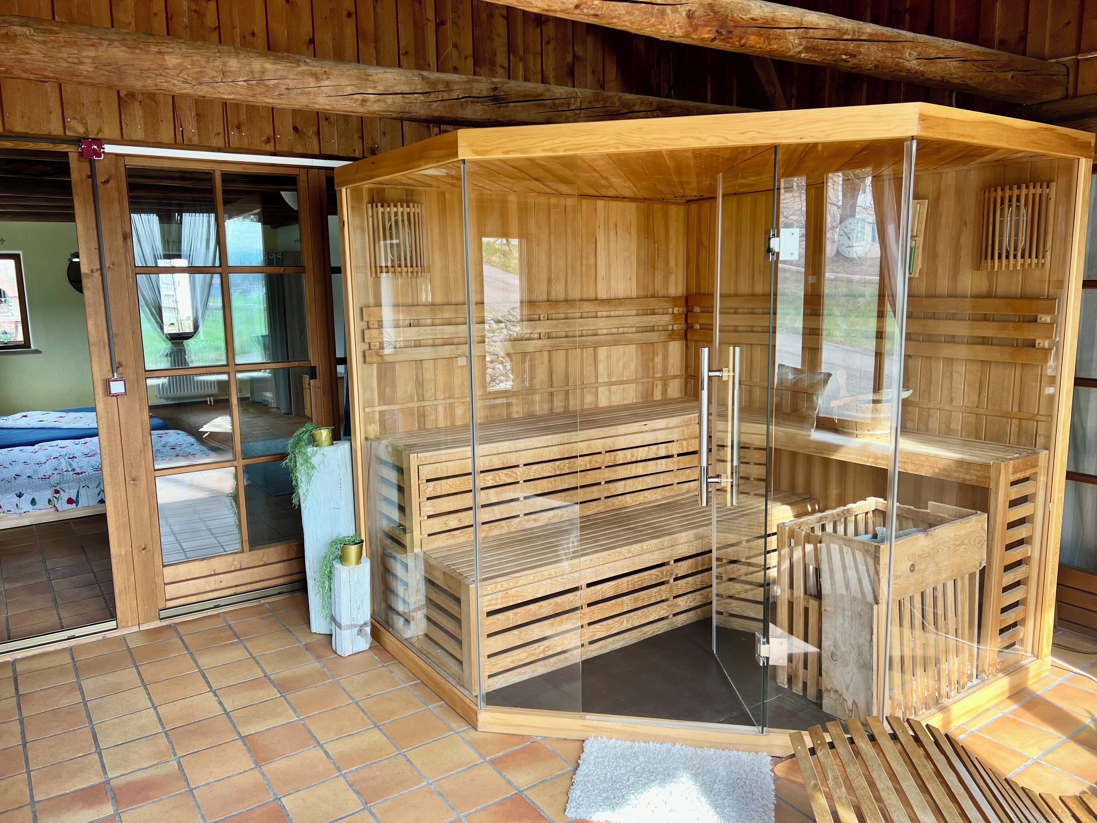 Eine Sauna mit Holzwänden und Glastüren, ein Bett mit blauer Bettdecke und ein gefliester Boden.