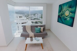 Ein modernes Wohnzimmer mit einem grauen Sofa, einem weißen Couchtisch und einem großen Fenster mit Blick auf die Stadt.