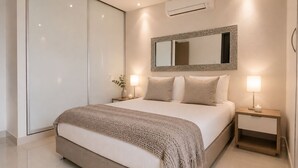 A modern bedroom with a large bed, bedside lamps, a mirror, and an air conditioning unit. - Neos Apartment – Near the Sea by SOHO – 303A (Santa Marta)