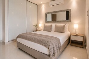 A modern bedroom with a large bed, bedside lamps, a mirror, and an air conditioning unit. - Neos Apartment – Near the Sea by SOHO – 303A (Santa Marta)