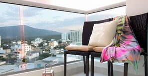 Un balcone con una sedia, un cuscino e vista su un panorama urbano che include edifici e montagne.