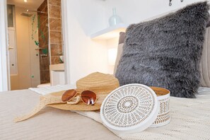 Ein Bett mit weißer Decke, einem Strohhut, Sonnenbrillen und einem weißen gewebten Korb.