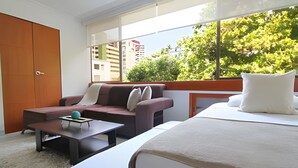 Una camera d'hotel moderna con divano, un tavolino, un letto e un'ampia finestra con vista su edifici e alberi.