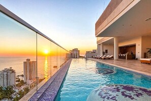 A rooftop infinity pool with a view of the sunset over the ocean, surrounded by modern buildings. - Ambar Roca Apartment – Near the Sea by SOHO – 353A (Santa Marta)