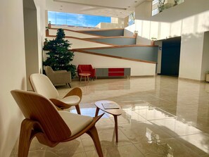 A spacious lobby with a high ceiling, a staircase, and a seating area with chairs and a table.