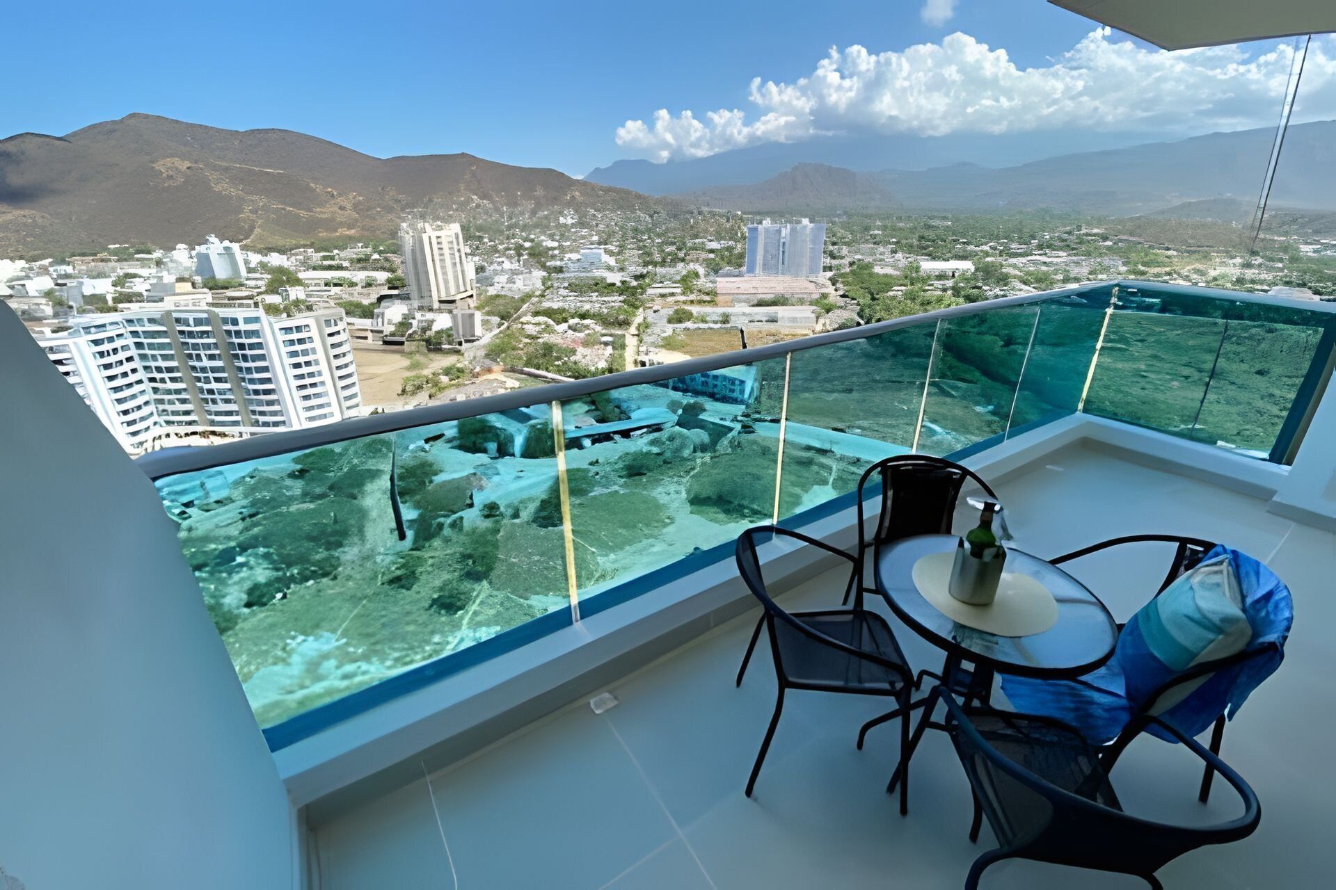 A balcony with a glass barrier overlooking a cityscape and mountains.