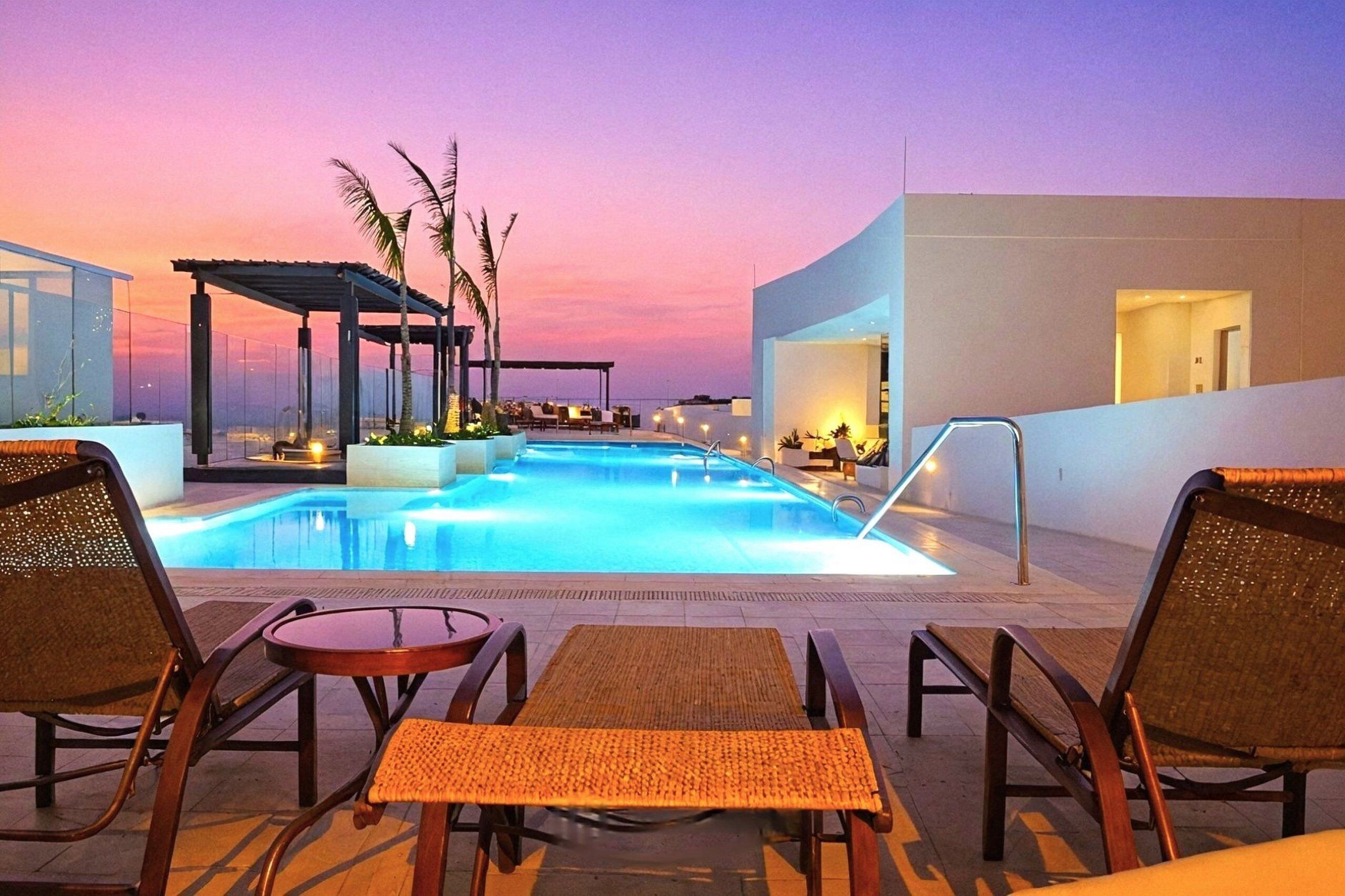 A pool area with lounge chairs and a covered seating area, surrounded by buildings.