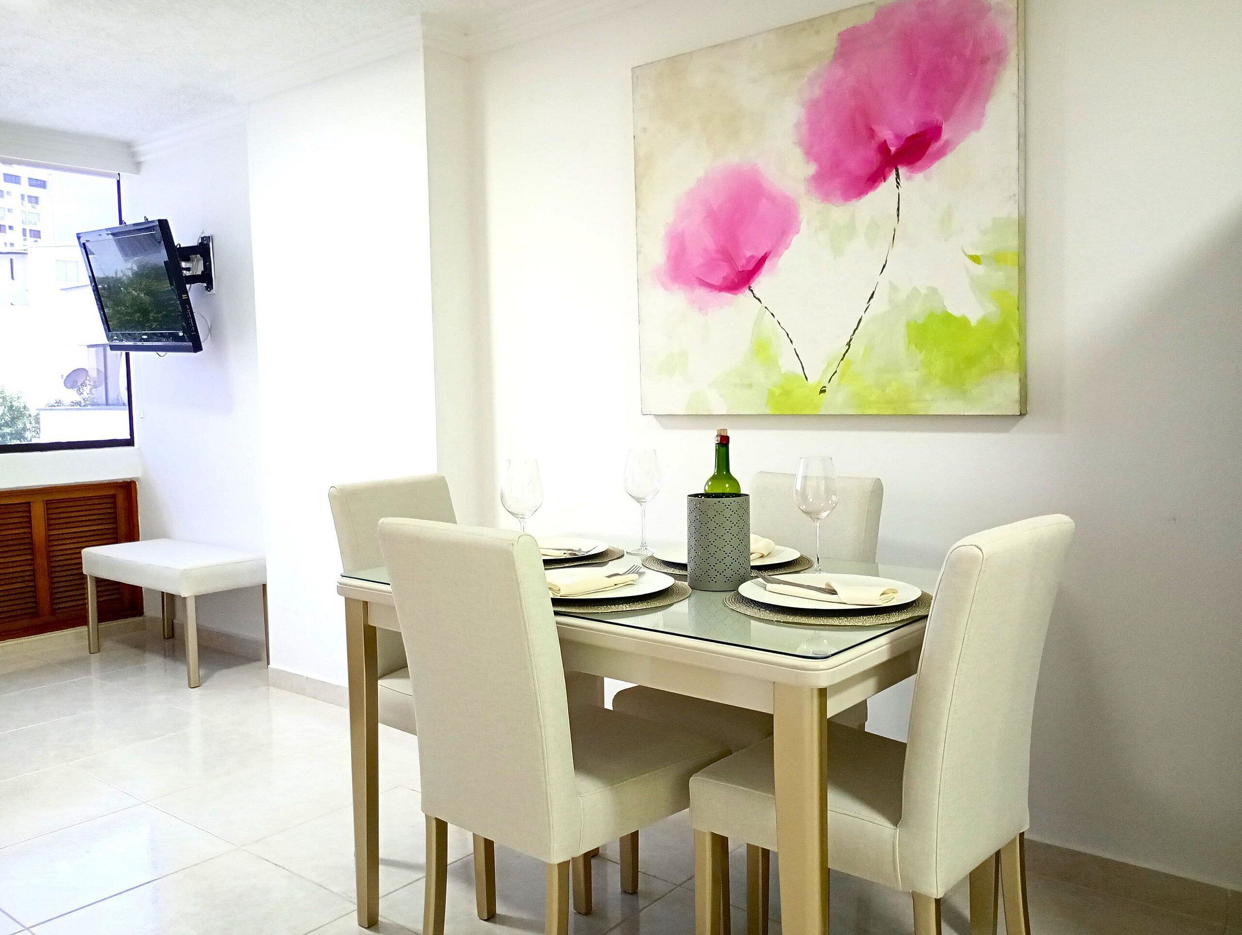 A dining area with a table set for four, chairs, a bottle of wine, and a television mounted on the wall.