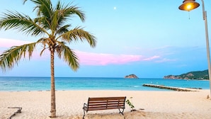 Una playa con una palmera, un banco y una farola.