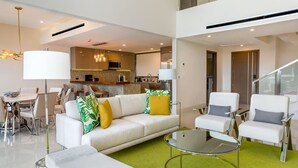 Ein modernes Wohnzimmer mit einer Couch, Sesseln, einem Glastisch und einem Essbereich mit Tisch und Stühlen.