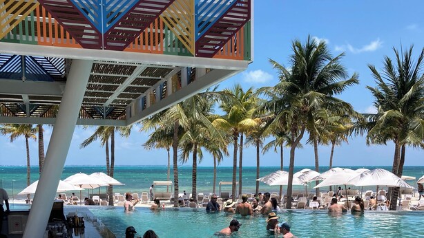 Ein Poolbereich mit klarem Wasser, Liegestühlen, Sonnenschirmen und Palmen.