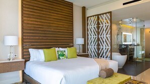 Ein modernes Hotelzimmer mit einem großen Bett, einem Nachttisch, einem Sessel und einem ein Glasfenster trennenden Badezimmer.