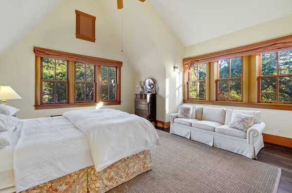 A bedroom with a large bed, a sofa, and a dresser. There are windows with curtains and a view of trees outside. - High Rock Ranch - The Luxury Private Estate in Yorkville (Yorkville)