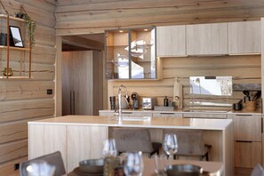 A modern kitchen with wooden cabinetry, a central island, and a dining area with chairs and wine glasses. - Skjønnhet Cottage: Luxury Cottage close to slopes (Ringebu)