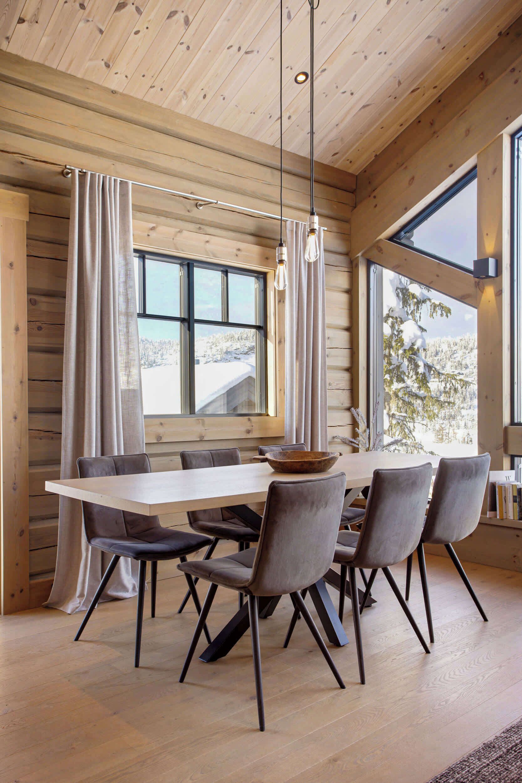 A wooden interior with a dining table, chairs, and large windows.