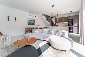 Ein modernes Wohnzimmer mit einem Ecksofa, einem Couchtisch und einer Treppe, die in eine Küche führt.
