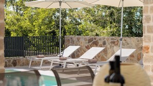 Ein Poolbereich mit Liegestühlen, Sonnenschirmen, einem Tisch mit Wein und Snacks sowie einer Steinmauer.
