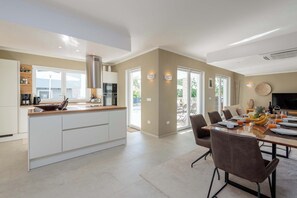 A modern kitchen with white cabinets, a central island, and a dining area with a table set for four. - Villa Mileni - Relaxing villa with pool + sauna (Farini)