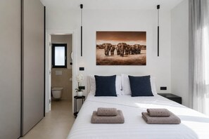 Una camera d'albergo moderna con un letto grande, un quadro con degli elefanti, un tavolino e un comodino.