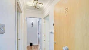 Een gang met een houten deur met de aanduiding '2', een lamp aan het plafond en een deurbel.
