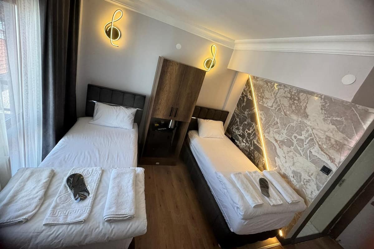 A hotel room with two beds, a marble accent wall, and a coat rack with towels.