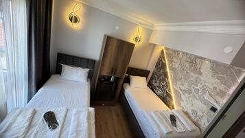 A hotel room with two beds, a marble accent wall, and a coat rack with towels.