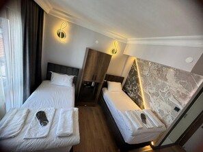 A hotel room with two beds, a marble accent wall, and a coat rack with towels.
