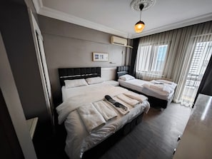 A hotel room with two beds, a ceiling light, an air conditioning unit, and a window with curtains.