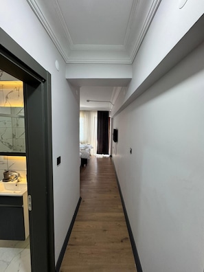 A narrow hallway with a wooden floor, white walls, and a door on the left.