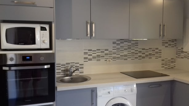 Een moderne keuken met grijze kastjes, een magnetron, een vaatwasser en een spoelbak.