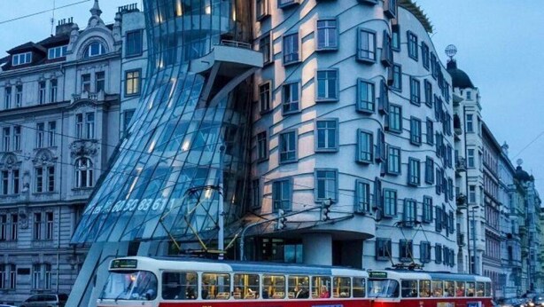 Un bâtiment moderne doté d’une façade en verre incurvée, avec un tramway devant.